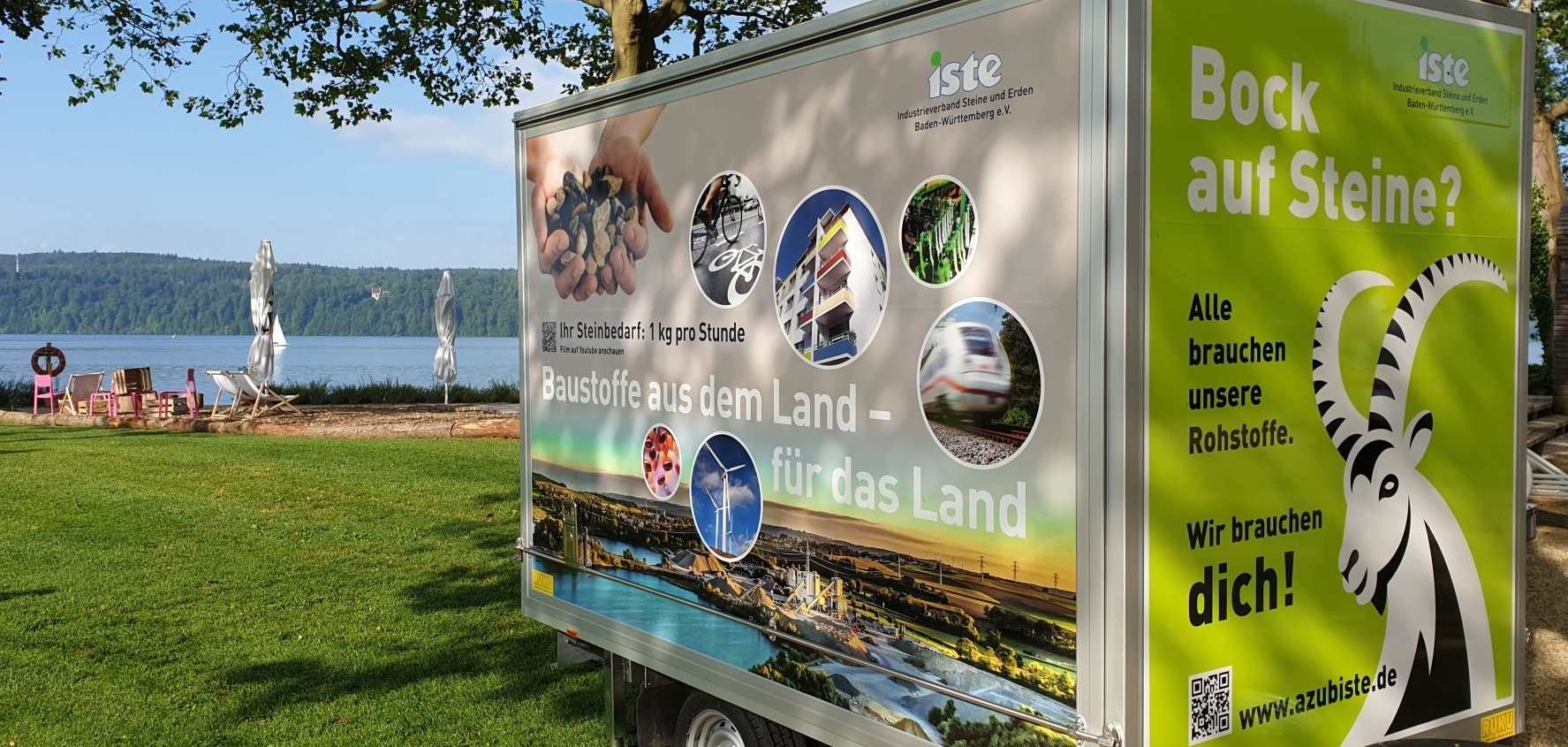 Ein Autoanhänger mit aufgedruckten Bildern steht am Ufer des Bodensees.
