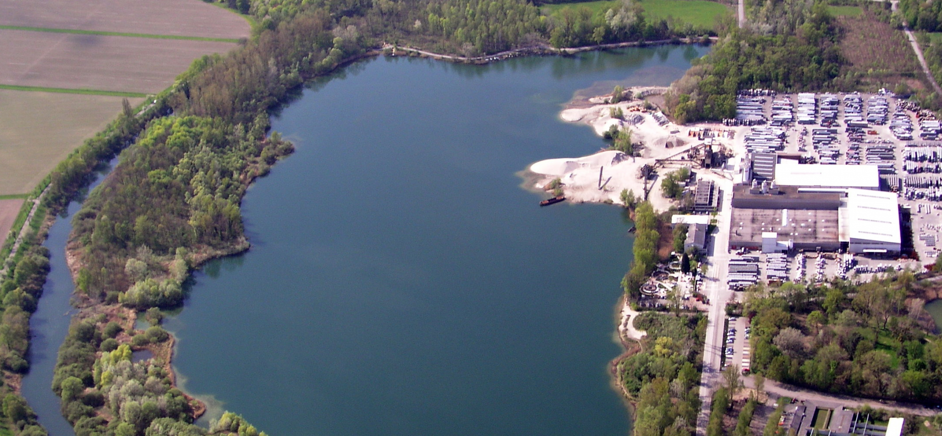 Ein Baggersee mit angrenzendem Kieswerk aus der Luftperspektive.